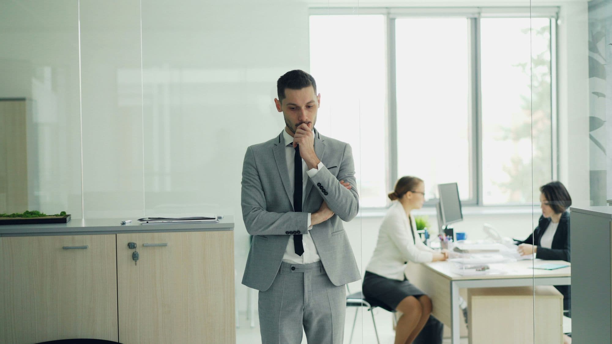 Businessman standing deep in thought in a modern glass-walled office